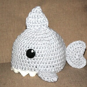 May include: A gray crocheted shark hat with a black button eye and white teeth.