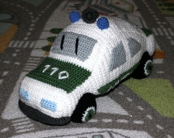 May include: A crocheted toy police car with a green and white body, blue and white lights on top, and the number 110 on the side.