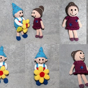 May include: Two crocheted figures, one wearing a blue hat and the other with brown hair, holding yellow flowers with red centres. The figures are standing on a grey textured surface.