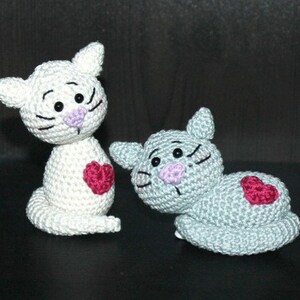 May include: Two crocheted cat toys, one white and one gray, with pink noses and black eyes. Each cat has a red heart sewn on its chest.