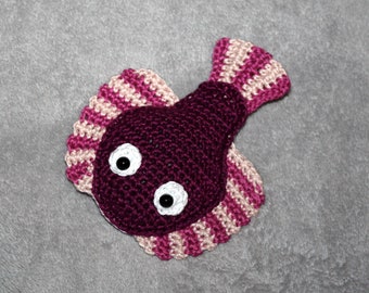 May include: A crocheted fish toy with pink and purple stripes. The fish has large white eyes with black pupils.