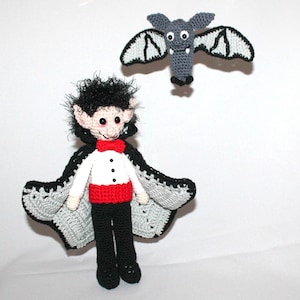 May include: A crocheted vampire doll wearing a black cape with a red bow tie and white shirt. The doll has black hair, pointy ears, and a red nose. A gray crocheted bat is flying above the doll.