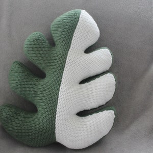 Puede incluir: Una almohada de forma de hoja hecha a crochet en verde y blanco. La almohada está hecha de hilo suave y tiene una superficie texturizada.