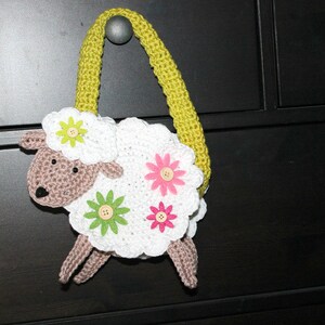 May include: A white crocheted lamb shaped bag with a green strap and pink and yellow flower accents.