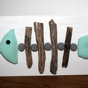 May include: A light blue crocheted fish skeleton with gray crocheted balls and brown driftwood sticks on a white wooden background.