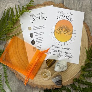 May include: A Gemini zodiac crystal set with Citrine, Howlite, Tiger Eye, and Agate stones. The set includes an orange organza bag and two cards with the Gemini symbol and stone properties. The stones are on a wooden slice.