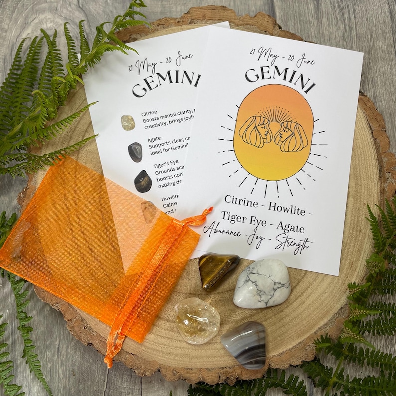 May include: A Gemini zodiac crystal set with Citrine, Howlite, Tiger Eye, and Agate stones. The set includes an orange organza bag and two cards with the Gemini symbol and stone properties. The stones are on a wooden slice.