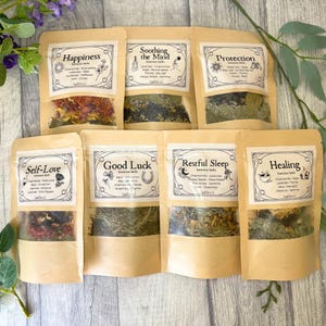 May include: Seven kraft paper pouches with clear windows, each labelled with a different intention: Happiness, Soothing the Mind, Protection, Self-Love, Good Luck, Restful Sleep, and Healing. The pouches contain dried herbs and flowers.