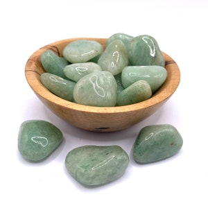 May include: A bowl filled with smooth, light green tumbled stones. The stones are in a wooden bowl and there are a few more stones scattered around the bowl.