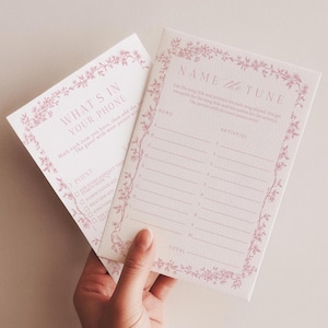 Può includere: Due carte da gioco rettangolari con un bordo floreale rosa polvere. Una carta è intitolata Name the Tune con righe numerate per canzone e artista. L'altra carta è intitolata What's in Your Phone con un elenco di controllo.