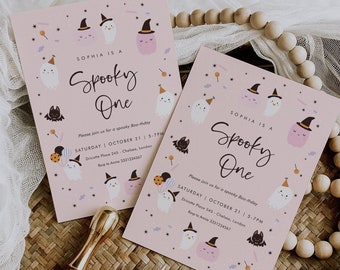 May include: Two pink Halloween-themed invitations with the text "Sophia is a Spooky One." The invitations feature illustrations of ghosts, bats, and stars. The invitations are on a woven surface with wooden beads.