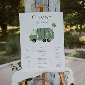 May include: A green and yellow illustrated garbage truck with a white background. The text "Oliver my first year" is at the top of the poster. The poster also includes information about Oliver's first year, including his weight, height, and favorite foods.