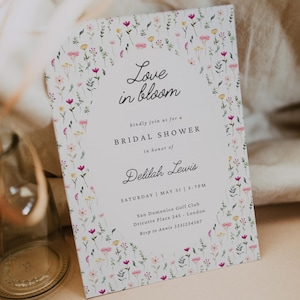 Può includere: Un invito floreale per un baby shower con il testo "Love in bloom" e i dettagli per il baby shower di Delilah Lewis. L'invito presenta uno sfondo bianco con un delicato bordo floreale.