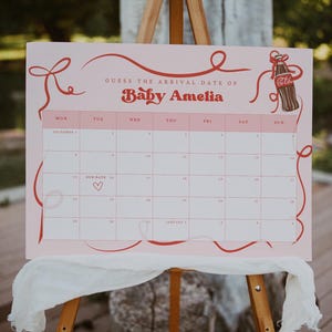 Può includere: Un calendario rosa con la scritta "Indovina la data di arrivo di Baby Amelia" in rosso. La griglia del calendario è rosa chiaro con dettagli rossi e un'illustrazione di una bottiglia di Coca-Cola. Un panno bianco è drappeggiato sotto.