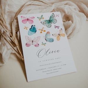 May include: A white invitation card with a watercolor butterfly design. The text on the card reads "Olivia is turning one! Please join us for a fluttering party Saturday | January 21 | 5-7PM Dricotte Place 245 - Chelsea, London Rsvp to Annie 3331234567"