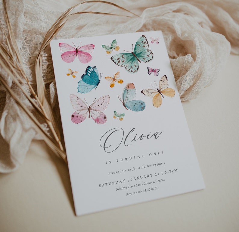 May include: A white invitation card with a watercolor butterfly design. The text on the card reads "Olivia is turning one! Please join us for a fluttering party Saturday | January 21 | 5-7PM Dricotte Place 245 - Chelsea, London Rsvp to Annie 3331234567"