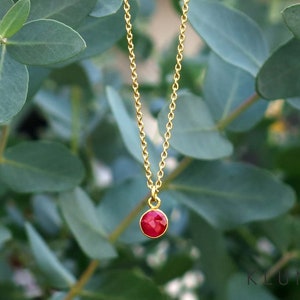Könnte beinhalten: Eine goldene Kettenkette mit einem kleinen, runden Anhänger aus rotem Edelstein.