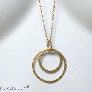 Könnte beinhalten: Goldkette mit einem Doppelkreis-Anhänger. Die Kreise sind texturiert und haben eine gehämmerte Oberfläche.