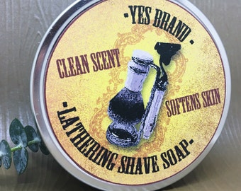 May include: A silver tin with a yellow label that reads "YES BRAND - LATHERING SHAVE SOAP - CLEAN SCENT - SOFTENS SKIN". The label features a vintage-style illustration of a shaving brush and a bottle of shaving soap.