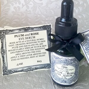 Pode incluir: Uma pequena garrafa de vidro de s&eacute;rum para os olhos Plum and Rose com conta-gotas preto e la&ccedil;o preto. Um cart&atilde;o com o nome e a descri&ccedil;&atilde;o do produto est&aacute; ao lado da garrafa. O r&oacute;tulo diz "Yes Organic Boutique and Spa".
