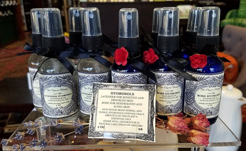 Puede incluir: Seis peque&ntilde;os frascos de vidrio con tapas de pulverizaci&oacute;n negras y etiquetas. Los frascos est&aacute;n dispuestos en una fila sobre una superficie de vidrio. Las etiquetas son blancas con texto negro y presentan un dise&ntilde;o floral. Los frascos est&aacute;n atados con una cinta negra y decorados con peque&ntilde;as flores rojas. Los frascos est&aacute;n etiquetados como "Lavender Hydrosol" y "Rose Hydrosol". Un cartel delante de los frascos dice "Hydrosols Lavanda para pieles sensibles y con problemas Rosa para pieles deshidratadas y envejecidas -Nuestros hidrolatos herbales y florales hechos en casa contienen trazas de aceites esenciales de la planta Agitar bien (la separaci&oacute;n es natural) y rociar en cualquier momento 2 oz 88"