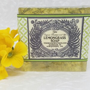 Puede incluir: Una barra de jabón de hierba de limón envuelta en papel estampado verde y blanco. La etiqueta dice "Yes Organic Boutique and Spa Lemongrass Soap yesorganicboutique.com Handmade in Albuquerque, NM."