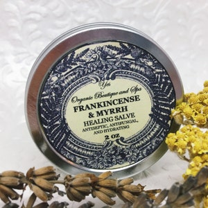 May include: A silver tin with a label that reads "Yes Organic Boutique and Spa Frankincense & Myrrh Healing Salve Antiseptic, Antifungal, and Hydrating 2 oz."