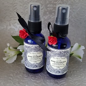 Puede incluir: Dos botellas de vidrio azul de 2 onzas con tapas de pulverizaci&oacute;n negras y lazos de cinta negra. Las botellas contienen hidrosol de rosa y est&aacute;n etiquetadas "Yes Organic Boutique and Spa Rose Hydrosol Handmade in Albuquerque, NM yesorganicboutique.com 2 oz."