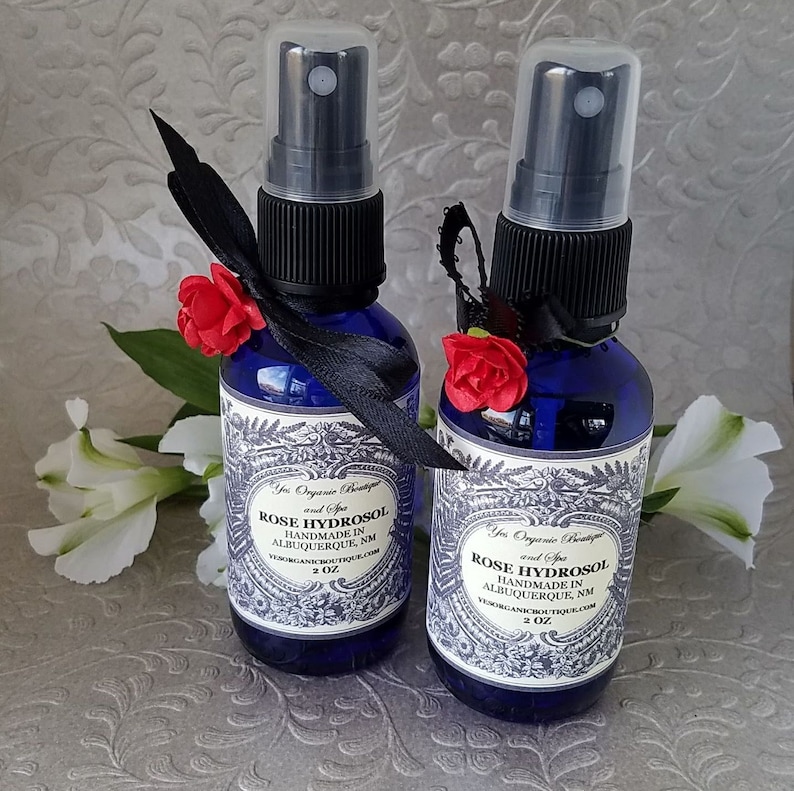 Puede incluir: Dos botellas de vidrio azul de 2 onzas con tapas de pulverizaci&oacute;n negras y lazos de cinta negra. Las botellas contienen hidrosol de rosa y est&aacute;n etiquetadas "Yes Organic Boutique and Spa Rose Hydrosol Handmade in Albuquerque, NM yesorganicboutique.com 2 oz."