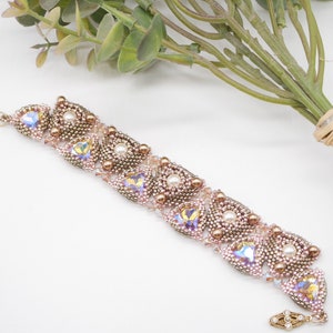 Pode incluir: Um delicado bracelete de contas com um design em ouro rosa e pérolas. O bracelete apresenta uma série de formas de lágrima entrelaçadas com cristais iridescentes e pequenos acentos de pérolas.