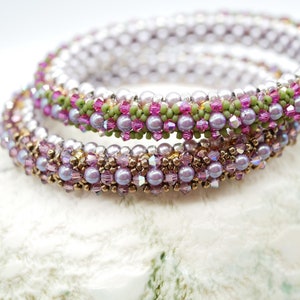 May include: A set of three beaded bracelets with a pink, green, and gold color scheme. The bracelets are made with small, round beads and are stacked on top of each other.