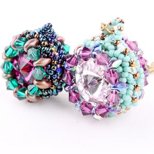 May include: Two beaded pendants with crystal centrepieces. The pendant on the left is green, purple, and copper. The pendant on the right is turquoise, pink, and clear.