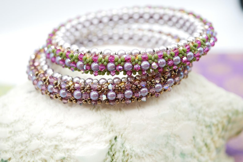 May include: A set of three beaded bracelets with a pink, green, and gold color scheme. The bracelets are made with small, round beads and are stacked on top of each other.