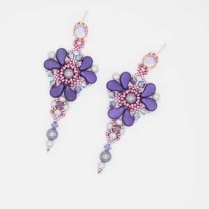 Puede incluir: Un par de pendientes colgantes con un diseño de flor morada. Los pendientes están hechos con cuentas moradas, rosadas y plateadas.