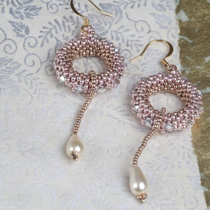 Op de afbeelding: Een paar gouden oorbellen met roze en heldere kralen, elk met een parel hanger.