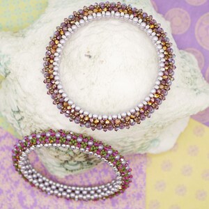 May include: Two beaded bracelets, one with purple and gold beads and the other with green and purple beads, are displayed on a white seashell.