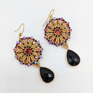 Könnte beinhalten: Goldene Ohrhänger mit einem schwarzen tropfenförmigen Stein und einem Perlenblumenmuster mit roten, violetten und goldenen Perlen.