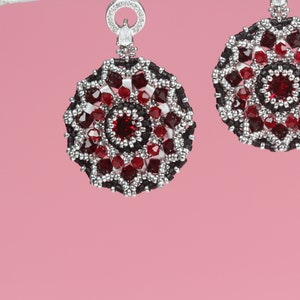 May include: A pair of silver earrings with red and black beaded designs. The earrings are round and have a floral pattern.