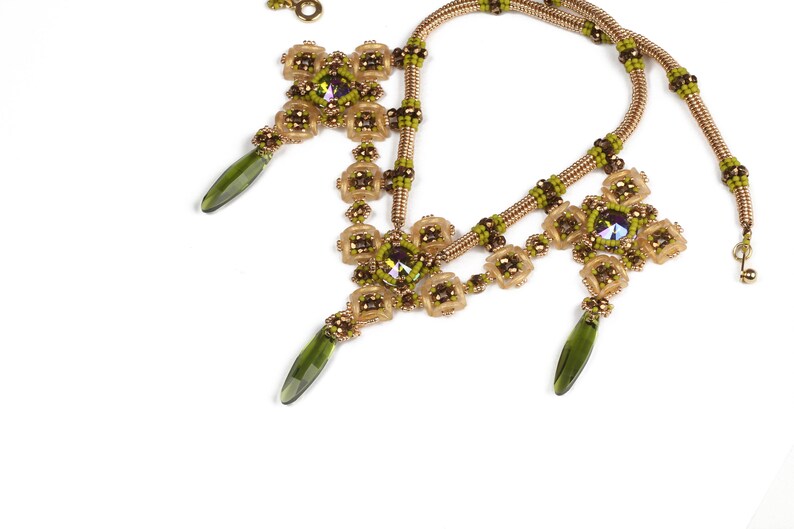 May include: A gold and green beaded necklace with three pendant drops. The necklace features a geometric design with a central crystal.