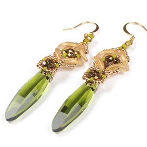 May include: A pair of green and gold dangle earrings with a geometric design. The earrings feature a teardrop-shaped green crystal and gold beads.