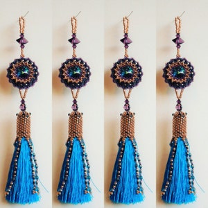 Peut inclure: Quatre boucles d'oreilles en forme de pompon avec un design en perles de couleur violette et cuivre et un pompon bleu.