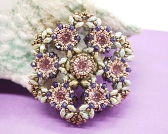Könnte beinhalten: Ein zartes Perlen-Anhänger mit floralem Design. Der Anhänger zeigt eine zentrale Gruppe aus rosa und violetten Perlen, die von kleineren weißen Perlen umgeben sind.