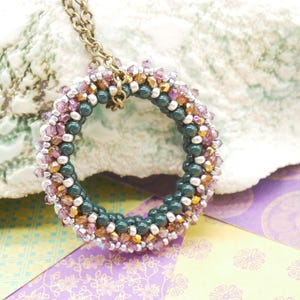 May include: A green, pink, and gold beaded necklace with a circular pendant. The pendant is made of small beads woven together in a circular pattern.