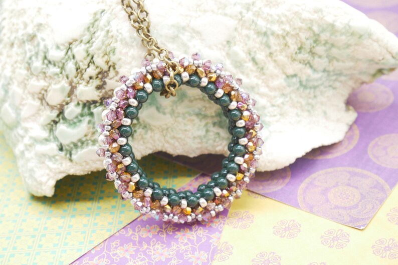 May include: A green, pink, and gold beaded necklace with a circular pendant. The pendant is made of small beads woven together in a circular pattern.