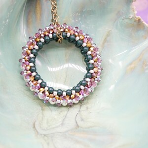 May include: A beaded necklace with a circular pendant made of green, pink, and gold beads. The pendant is hanging from a gold chain.