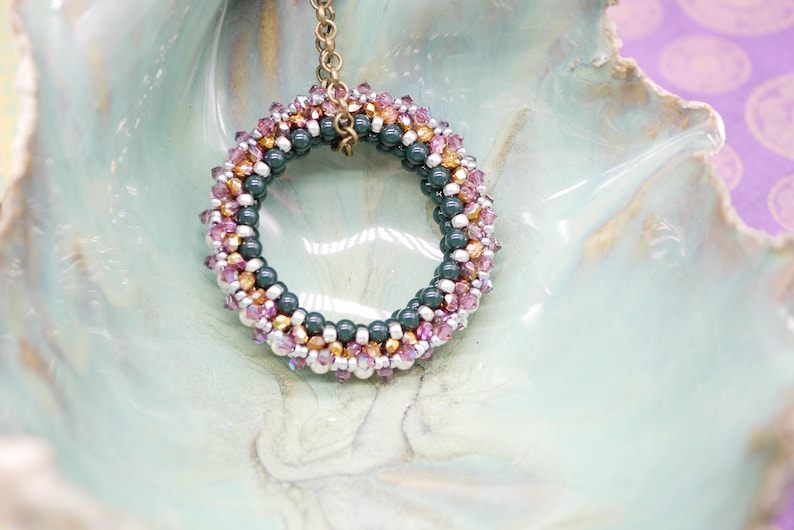 May include: A beaded necklace with a circular pendant made of green, pink, and gold beads. The pendant is hanging from a gold chain.