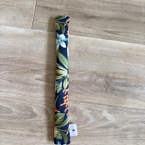 May include: A long, cylindrical fabric tube featuring a dark navy blue background with a botanical print of light blue flowers, green leaves, and orange coral-like branches. A small white rectangular fabric tag is attached to the lower side.