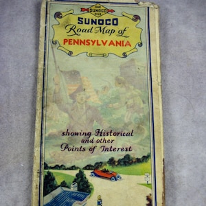 May include: Vintage Sunoco road map of Pennsylvania, featuring a colorful illustration of a car driving past a gas station and a historical scene with people holding an American flag. The map highlights historical points of interest.