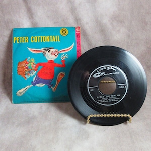 May include: A black 45 rpm record with a gold label that says "a little golden 45 record". The record is titled "Peter Cottontail" and is on a gold stand. The record cover is a colorful illustration of a rabbit holding a basket of eggs.