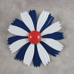 May include: A white and blue enamel flower brooch with a red center. The flower has a simple design with rounded petals.
